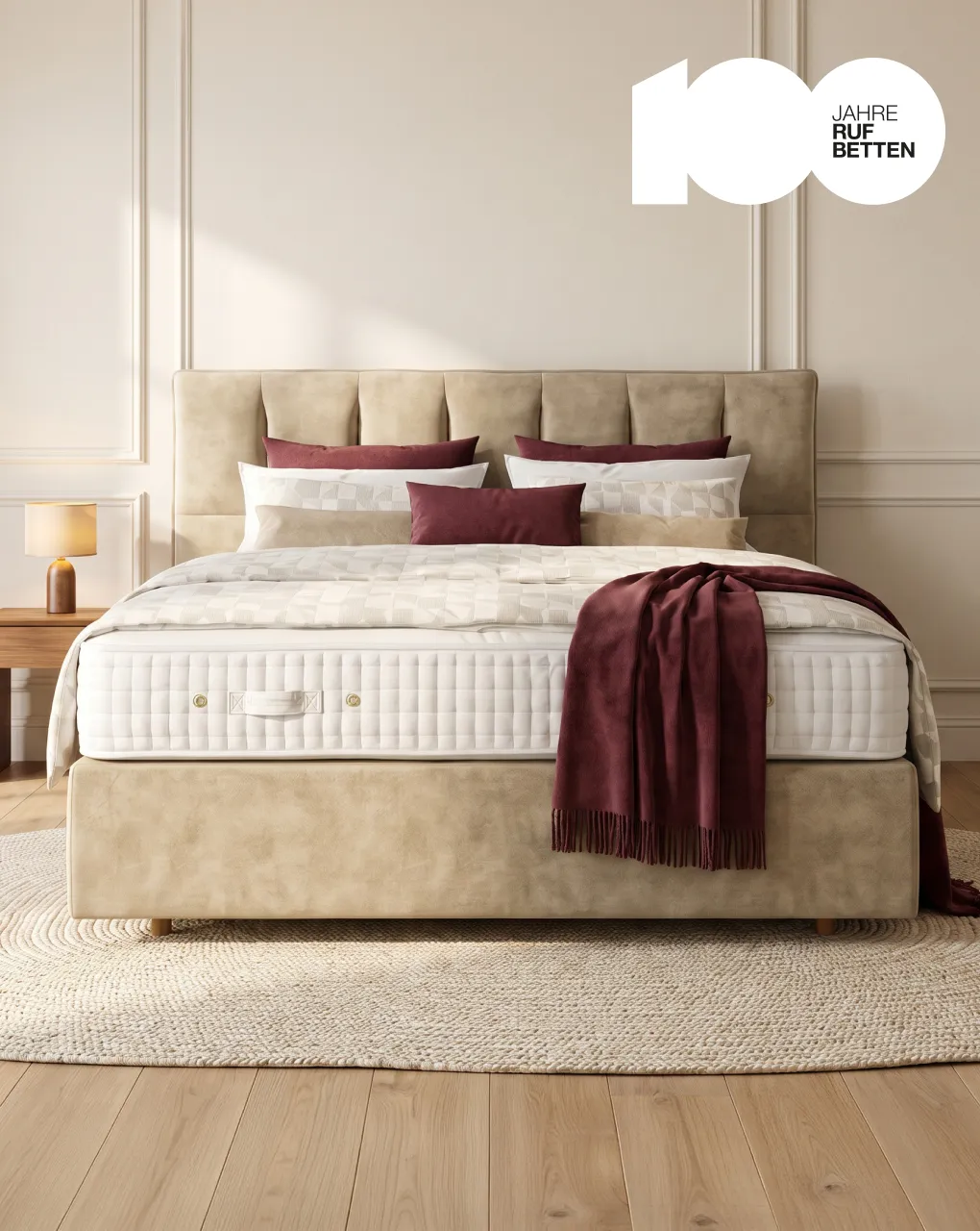 Boxspringbett von RUF Betten mit gestepptem Kopfteil und weinroter Decke in einem hellen Schlafzimmer